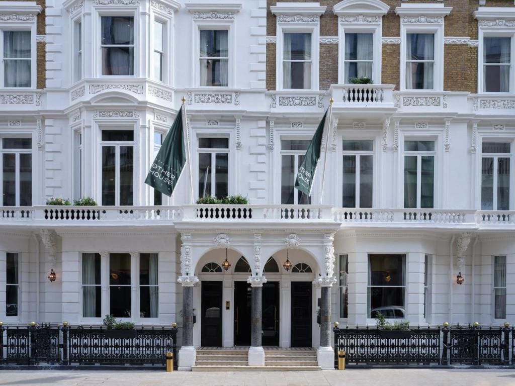 A white-painted, multi-storey building with ornate architectural details, large windows, black doors, and two green flags above the entrance reflects Naomi Heaton’s luxury branding and a sense of belonging.
